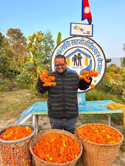 Founder Bal Bahadur Bista holding marigolds at the Sahara Ghar emblem, beneath the flag of Nepal